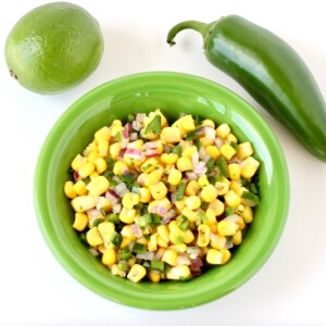 Green bowl of Corn Salsa with a pepper and a lime.