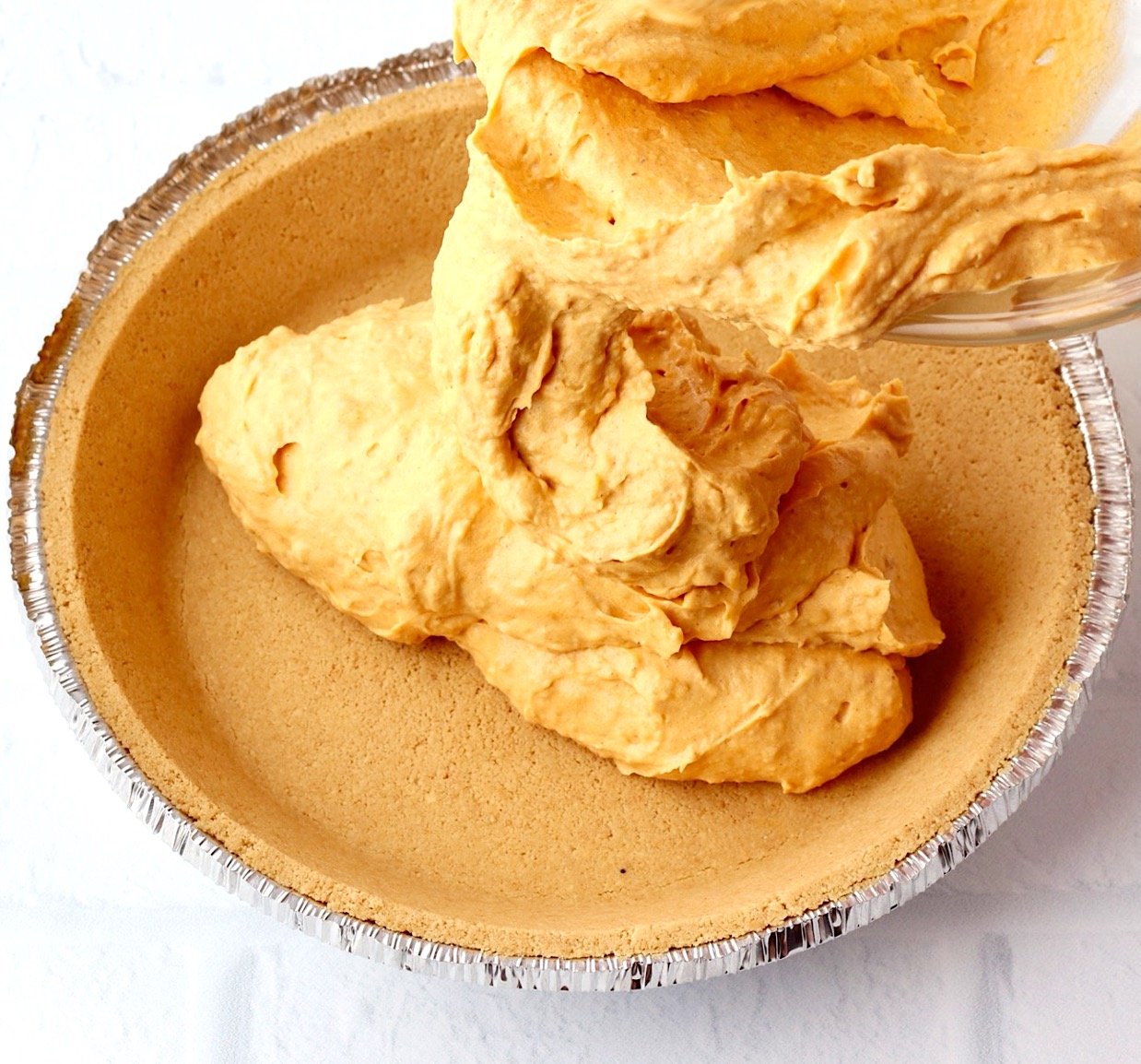 Pumpkin pie filling being poured into a graham cracker pie crust.