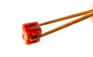Chopsticks holding a piece of General Tso chicken.
