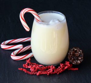 Candy cane in a glass of eggnog punch.