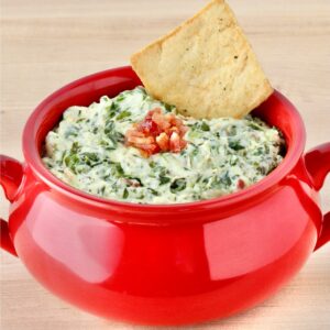 Spinach dip in red bowl with chip.