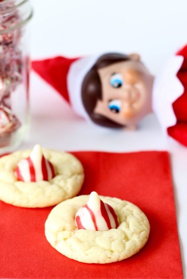 Two candy cane kiss cookies on napkin with elf in the background.