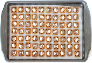Hershey hugs on square pretzels on a lined baking sheet.