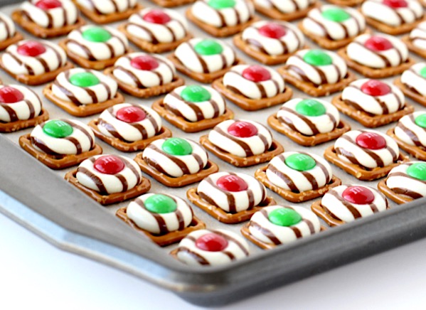 Christmas pretzel treats with Hershey hugs and M&M\'s on lined baking sheet.