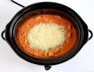 Shredded cheese over Tortellini Soup in a slow cooker.