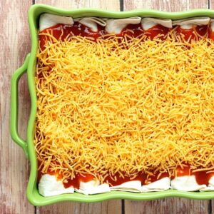 Beef enchiladas in casserole dish with enchilada sauce and shredded cheese on top.