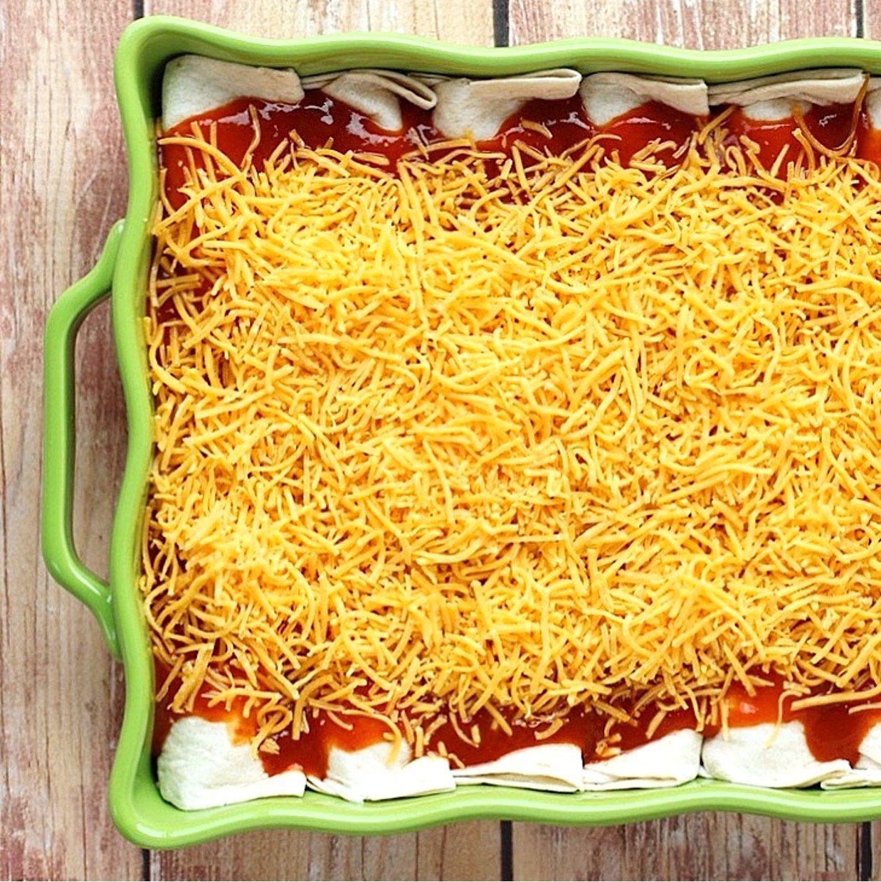 Beef enchiladas in casserole dish with enchilada sauce and shredded cheese on top.