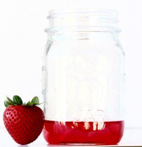 Strawberry next to a jar of strawberry syrup.