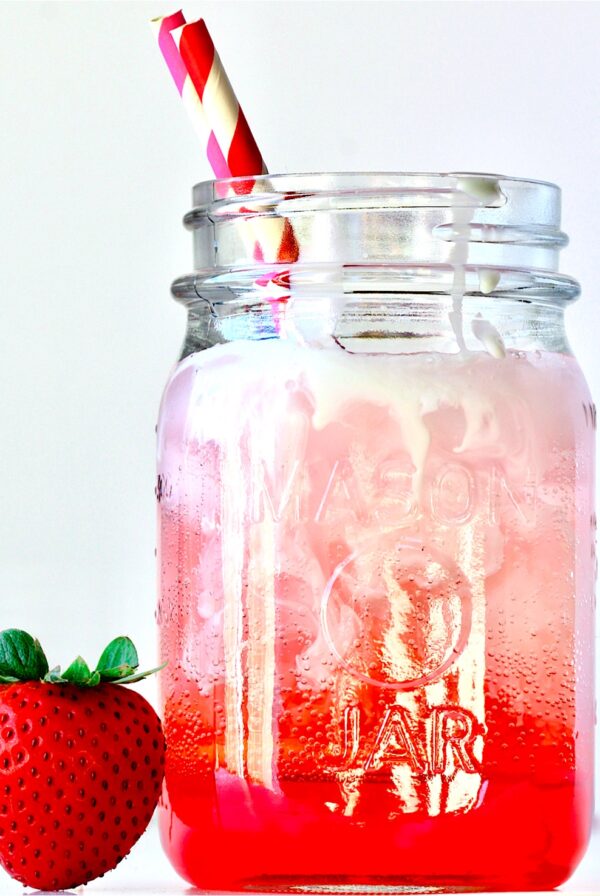 Italian soda in mason jar with straws and a strawberry to the side.