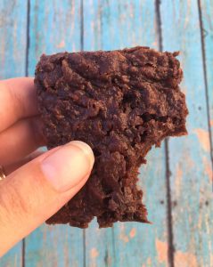 Person holding a brownie with a bite missing.