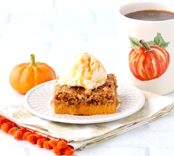 Slice of pumpkin dump cake on plate with vanilla ice cream scoop.