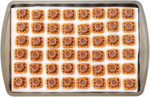 Rolos on square pretzels on a lined baking sheet.