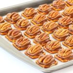 Turtles candy pieces with pretzels, pecans, and Rolos on cookie sheet.