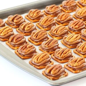 Turtles candy pieces with pretzels, pecans, and Rolos on cookie sheet.