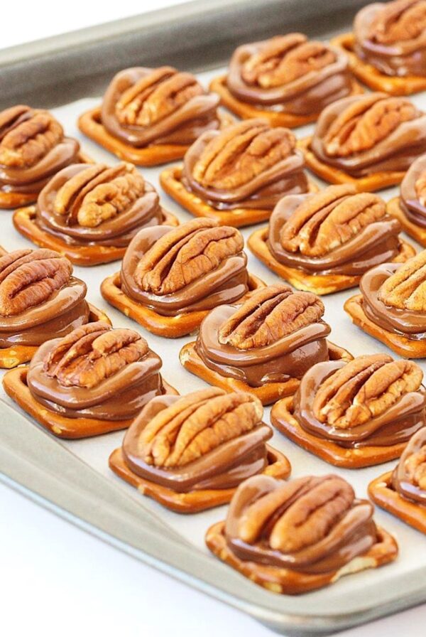 Turtles candy pieces with pretzels, pecans, and Rolos on cookie sheet.