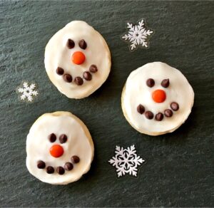 Three frosted snowman cookies decorated with chocolate chip eyes and mouths and m&m noses.