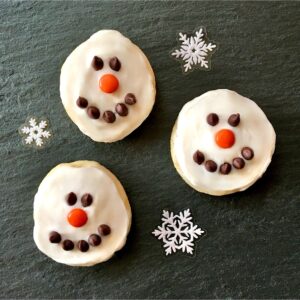Three frosted snowman cookies decorated with chocolate chip eyes and mouths and m&m noses.