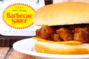 Cooked steak bites with barbecue sauce on bun with slice of cheese.