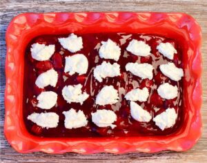 Baking dish of strawberry filling topped with cream cheese.