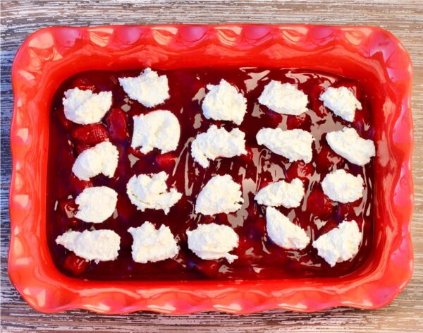 Baking dish of strawberry filling topped with cream cheese.