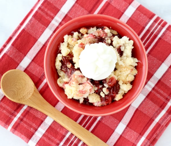 Baked Strawberry Dump Cake in red bowl with wooden spoon.
