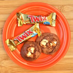 Chocolate Twix cookies on an orange plate with two Twix bars to the side.