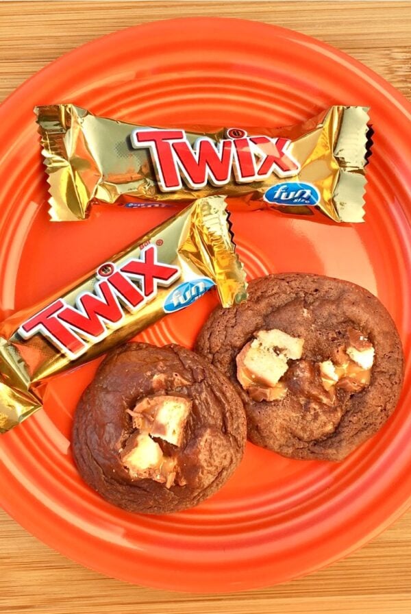 Chocolate Twix cookies on an orange plate with two Twix bars to the side.