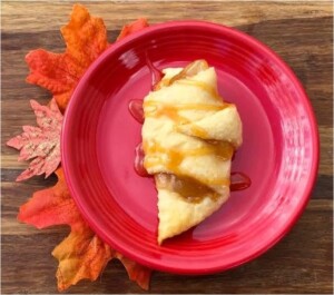 Baked caramel apple crescent roll on plate drizzled with caramel sauce.
