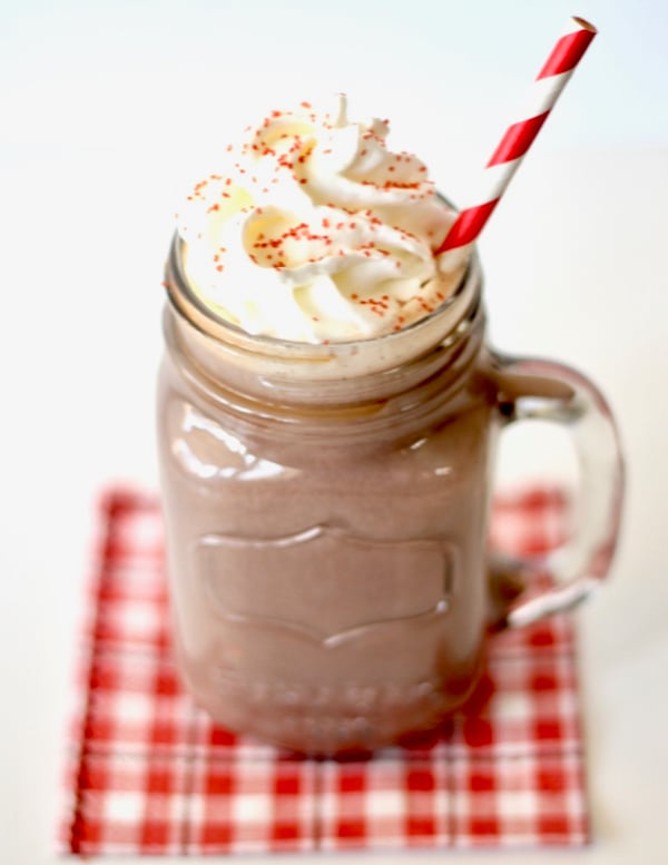 Peppermint hot chocolate in mason jar mug with whip cream and sprinkles on top.