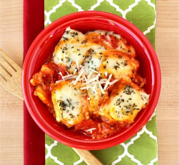 Red bowl of ravioli with sauce topped with cheese.