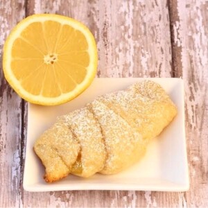 Baked lemon crescent roll on plate with powdered sugar on top.