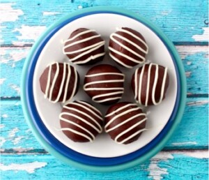 Chocolate oreo balls on plate drizzled with white chocolate. 