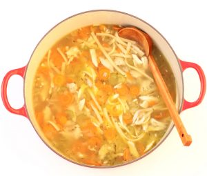 Wooden ladle in a Dutch oven of chicken noodle soup.