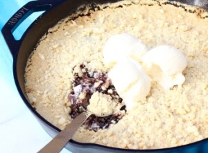 Baked blackberry crumble in skillet with scoops of ice cream on top.