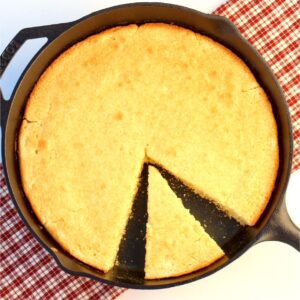 Baked cornbread partially sliced in cast iron skillet.
