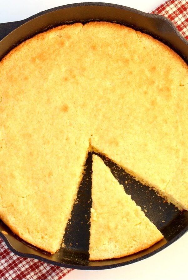 Baked cornbread partially sliced in cast iron skillet.