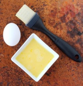 Bowl of egg wash with an egg and pastry brush.