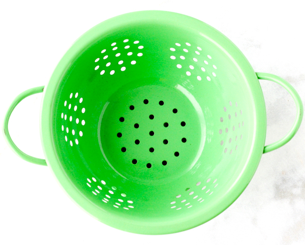 Green colander on a marbled surface.