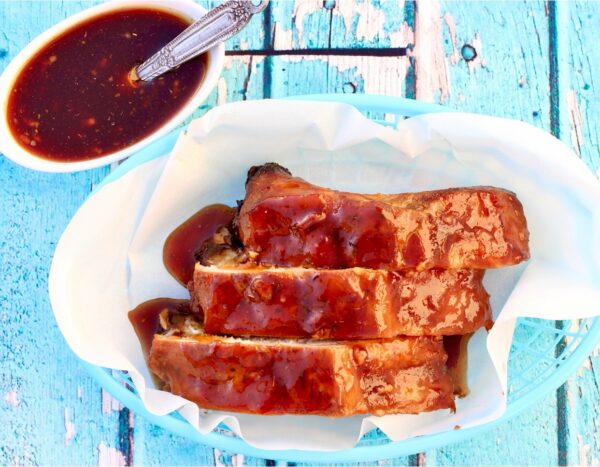 Three honey garlic ribs in basket with honey garlic sauce to the side.