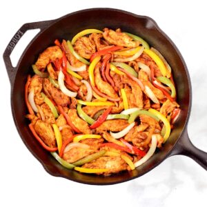 Chicken fajitas with bell peppers and onions in skillet.