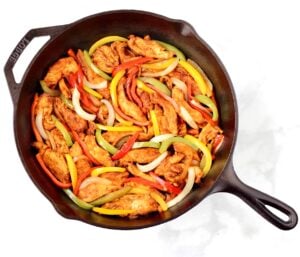 Cooked chicken fajitas in skillet with bell peppers and onions.