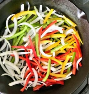 Bell peppers and onions saut&eacute;ing in skillet.