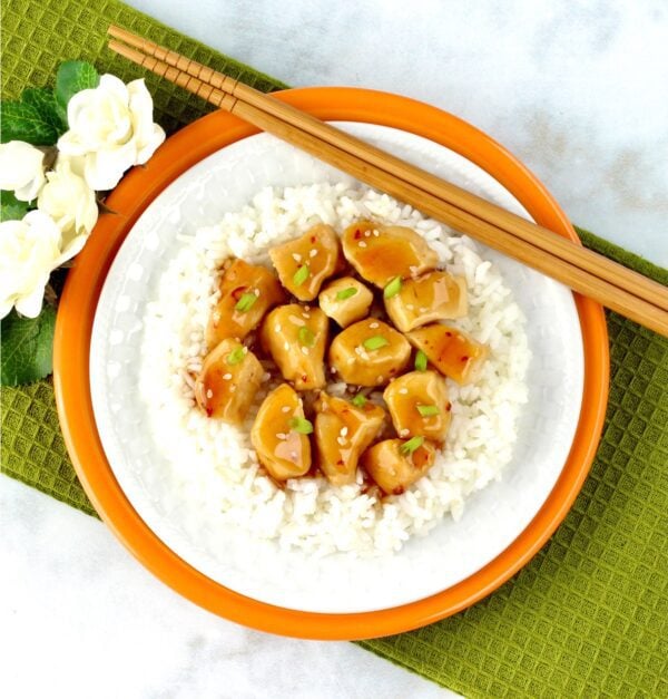 Rice, orange chicken, and chopsticks on a plate.