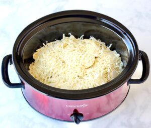 Alfredo ravioli topped with cheese in a Crock Pot.