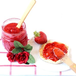 Strawberry Jam in mason jar with spoon and being spread on English muffin.