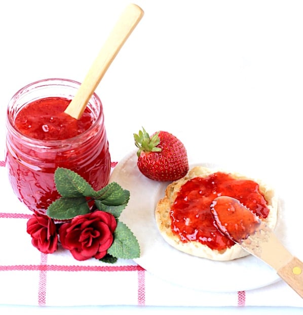 Strawberry Jam in mason jar with spoon and being spread on English muffin.