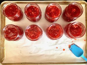 Strawberry jam in jars on a lined baking sheet.