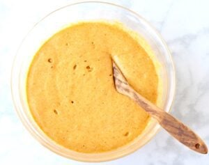 Wooden spoon in a bowl of pumpkin angel food cake batter.