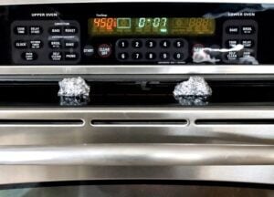 Balls of aluminum foil holding open an oven door.
