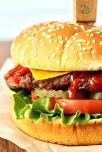 Burger with ketchup, cheese, pickles, tomato, and lettuce.